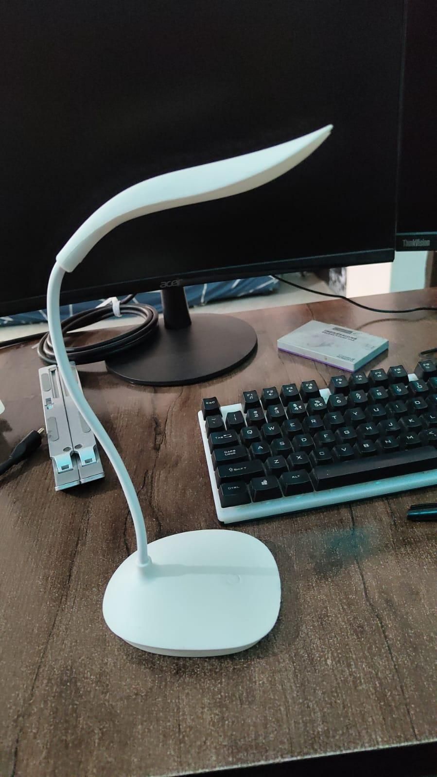 White LED desk lamp on a wooden desk with a computer monitor and keyboard in the background.