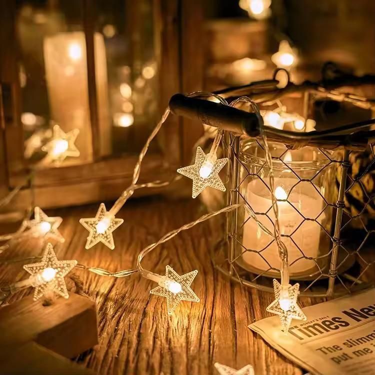 Star-shaped string lights next to a candle in a wire holder on a wooden surface.