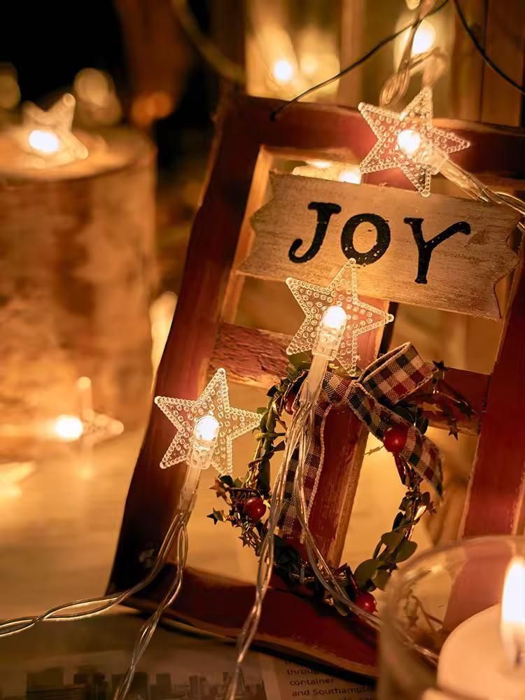 Decorative lantern with 'JOY' sign and star lights on a warm, blurred background.
