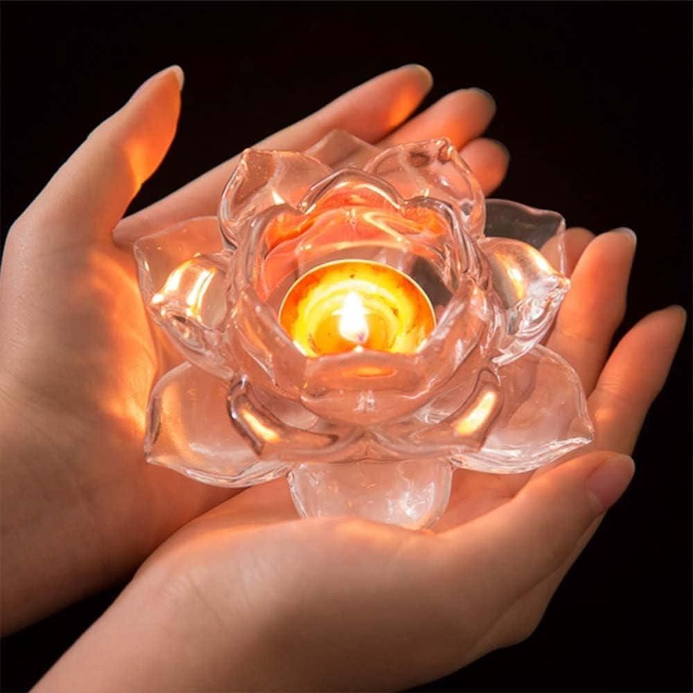 Clear glass lotus flower candle holder with a lit candle held in hands against a dark background